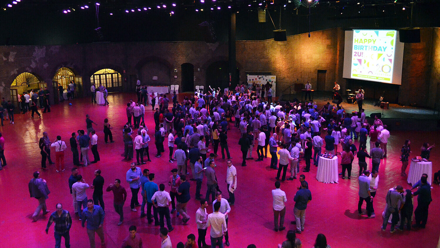 Multitud reunida en un gran salón de eventos interior con iluminación púrpura.