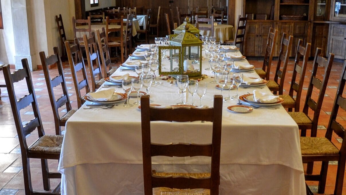 Derecha: Mesa larga preparada en interior con mantelería blanca, platos y copas listas para una cena.