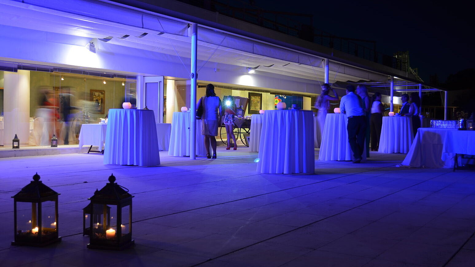 Centro: Evento nocturno en terraza iluminada con luces azules y mesas de cóctel.
