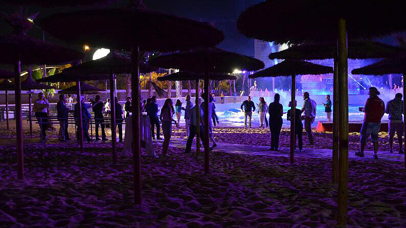 Derecha: Personas reunidas bajo sombrillas en una playa o piscina durante la noche con iluminación púrpura.