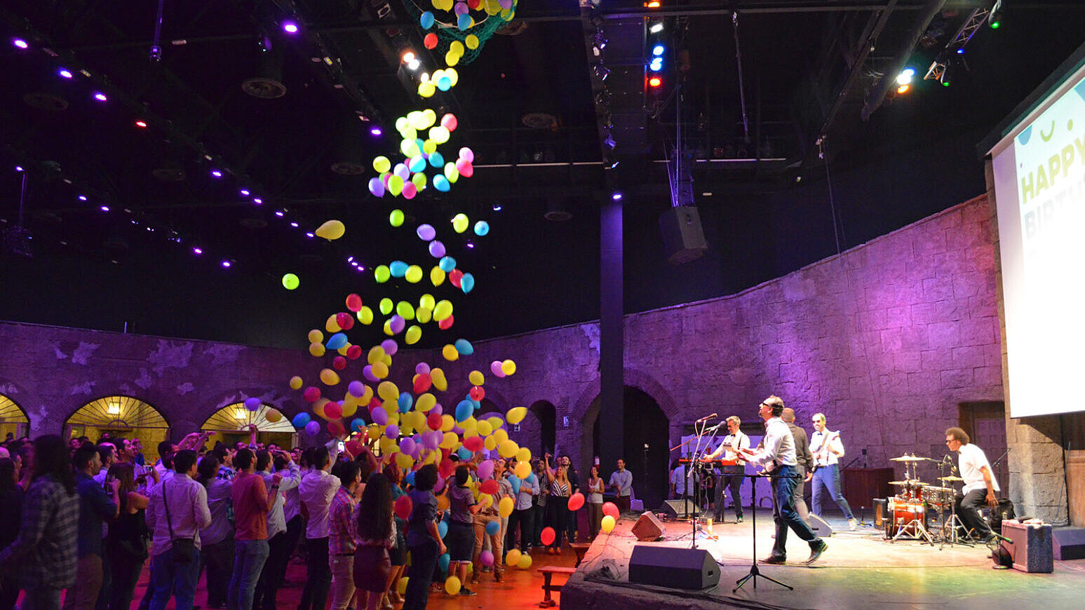 Derecha: Actuación en el escenario con músicos mientras caen globos de colores sobre el público.